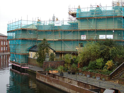 An image of scaffolding and green safety nets around a building next to a river