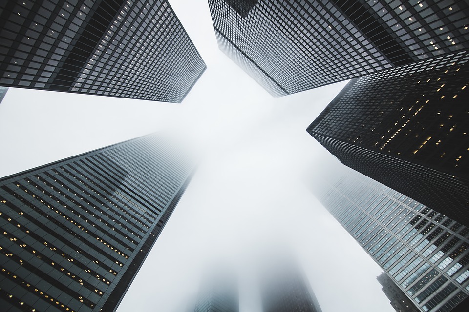 An image of looking up at multiple skyscrapers fading into fog